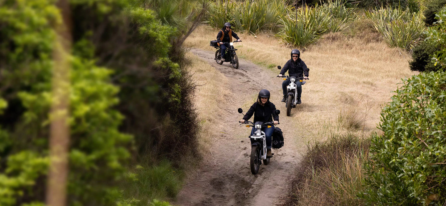 Three people enjoying a ride on the Adventure 2x2 UBCO along a sandy track through a brushy area